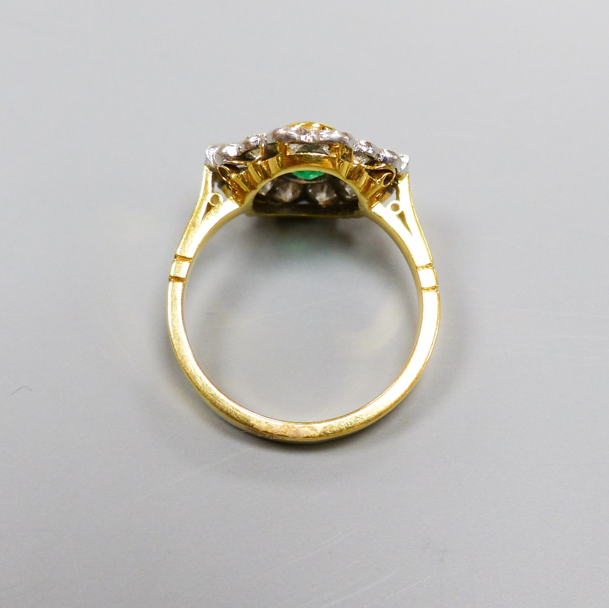 A modern 18ct gold, emerald, baguette and round cut diamond set shaped oval cluster ring, size L/M, gross weight 4.4 grams.